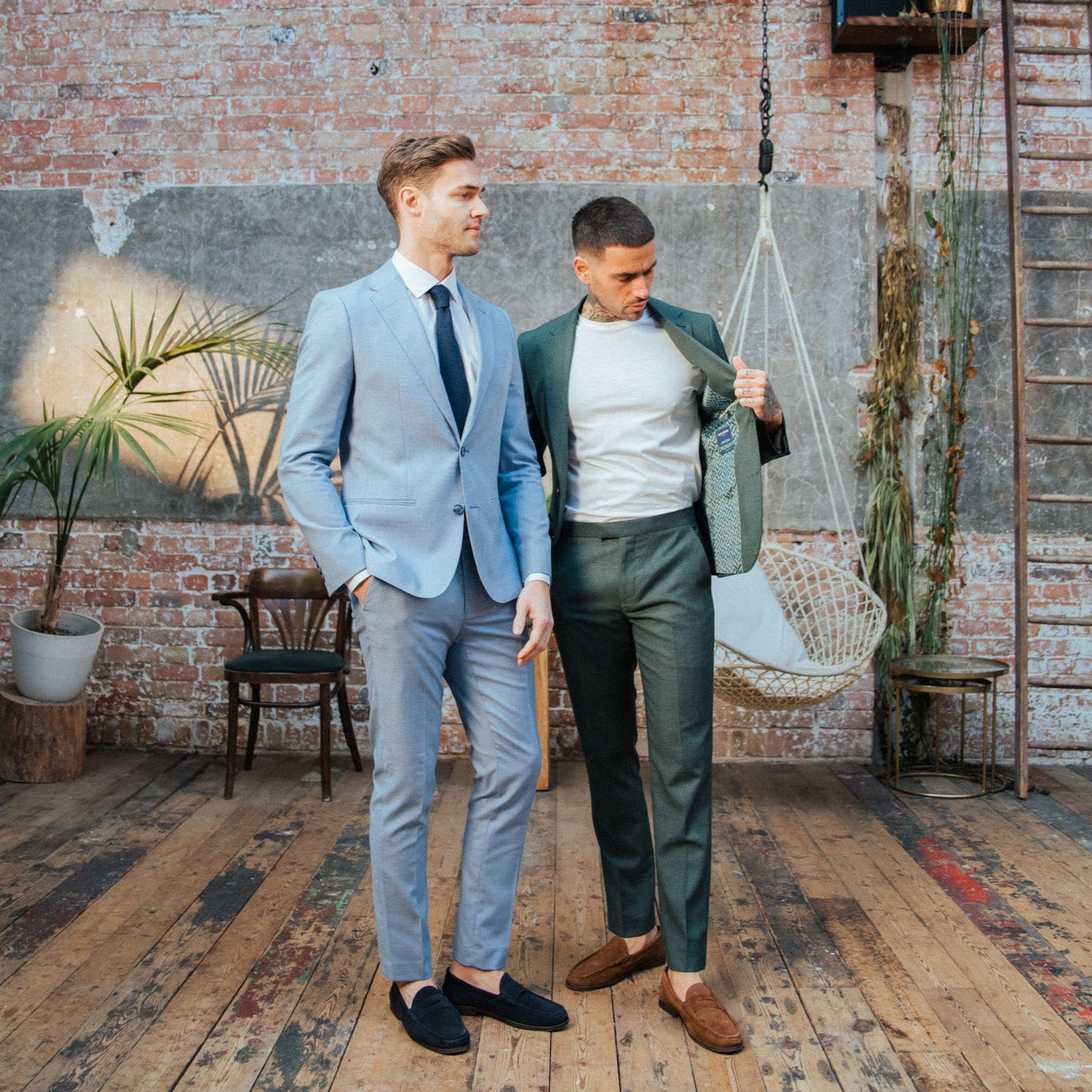 Two men in suits standing in a room with brick walls and wooden floors.